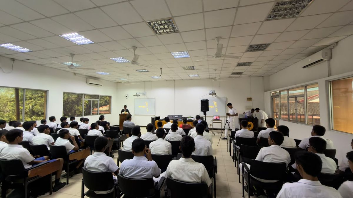 A classroom hall full of seated students facing a speaker at a lectern and a projection screen
