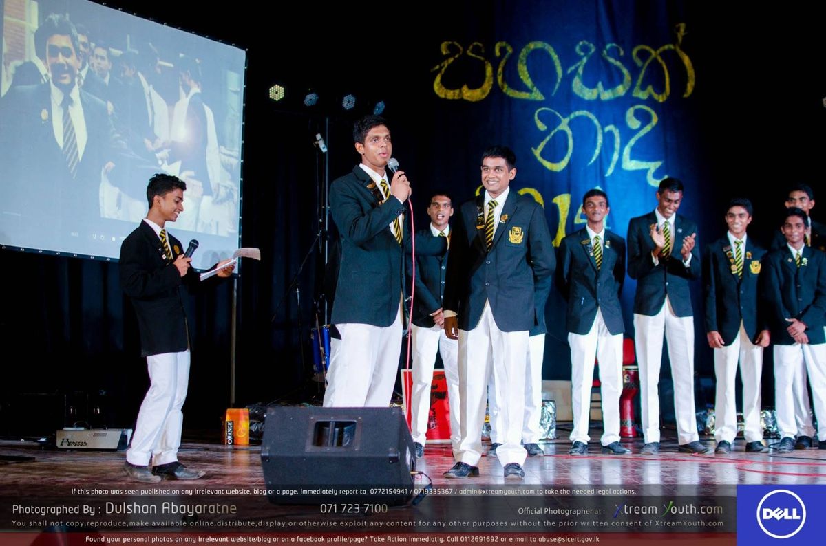 A presenter with a microphone introducing association members lined up on stage beside a projection screen